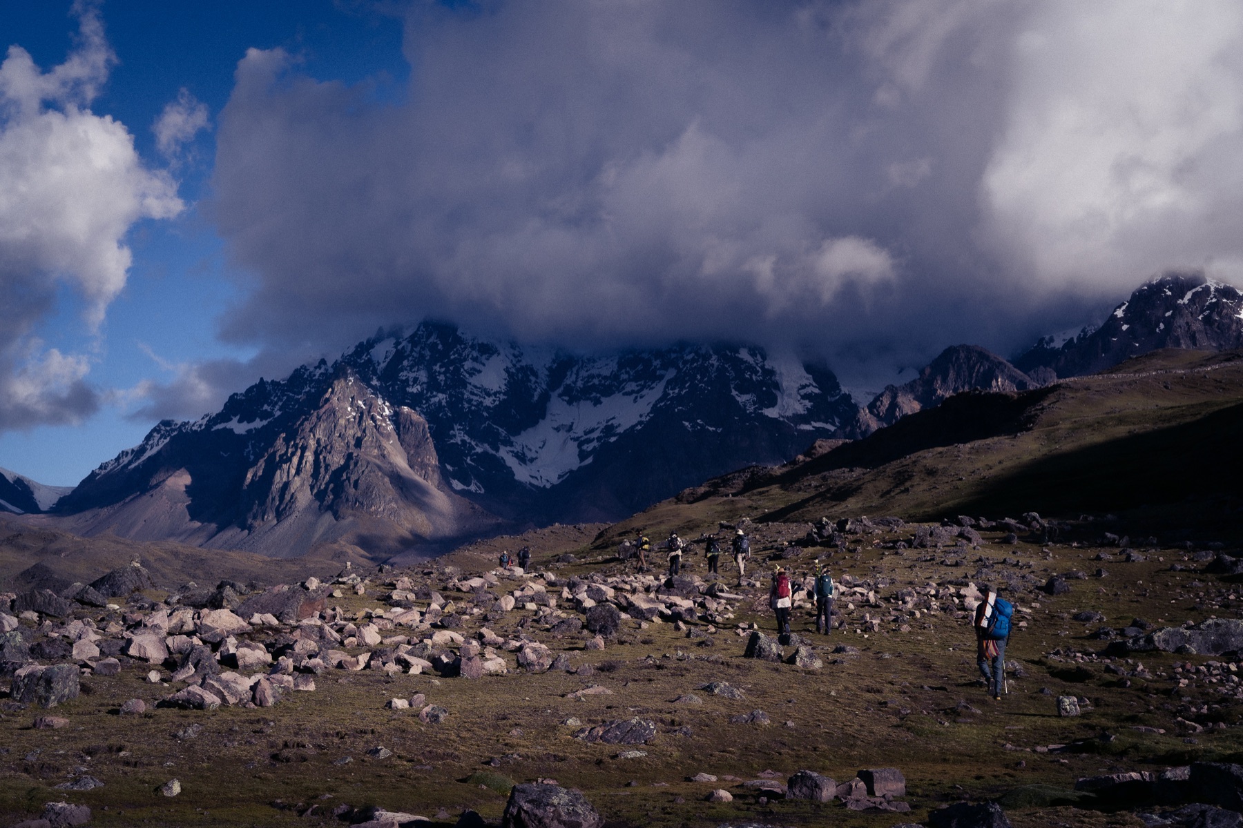 El grupo atraviesa un paisaje rocoso bajo las montañas y nubes del Ausangate.
