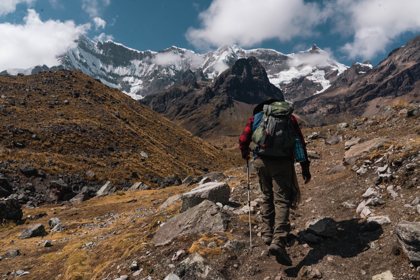 Un peregrino recorre el sendero entre rocas y montañas nevadas.