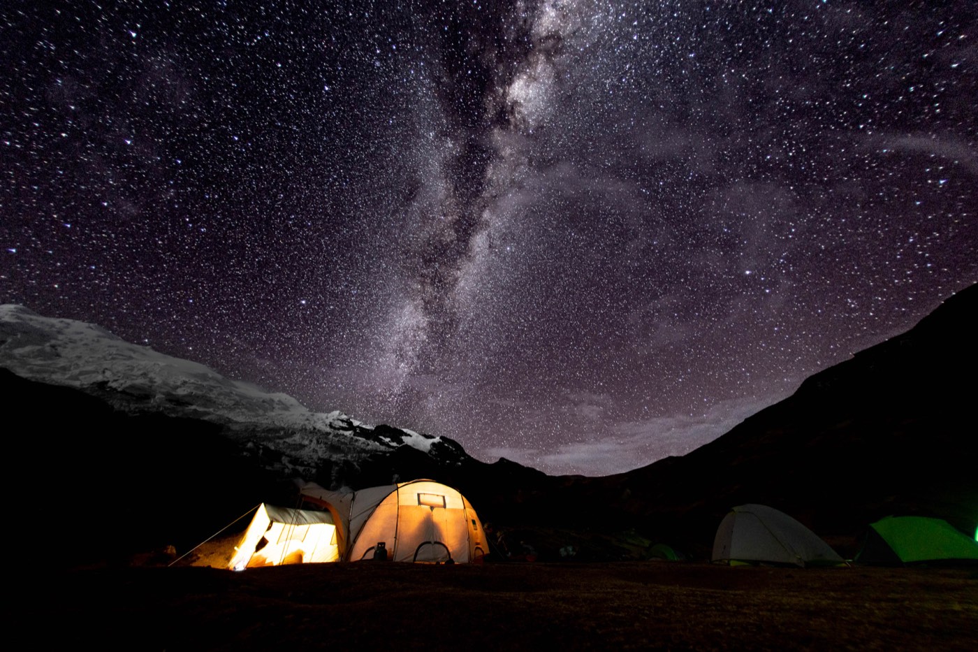 La Vía Láctea se extiende sobre un campamento iluminado en la cordillera.